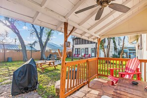 A covered patio with a ceiling fan, picnic tables, and red chairs.