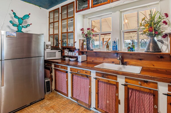 A kitchen with wooden cabinets, a stainless steel refrigerator, a microwave, and a sink. - Carriage Inn - Cottage (Bandera)