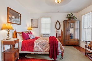 A bedroom with a bed, bedside lamps, a dresser, a mirror, and a window with blinds.