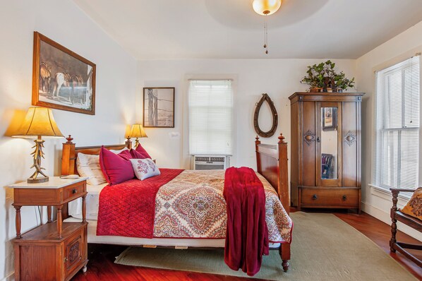 A bedroom with a bed, bedside lamps, a dresser, a mirror, and a window with blinds.