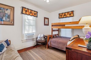 A bedroom with a bunk bed, a desk, a chair, a lamp, and a radiator.