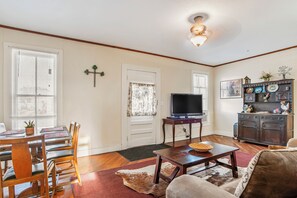 A living room with a television, wooden furniture, a dining area with a table and chairs, and a decorative cabinet.
