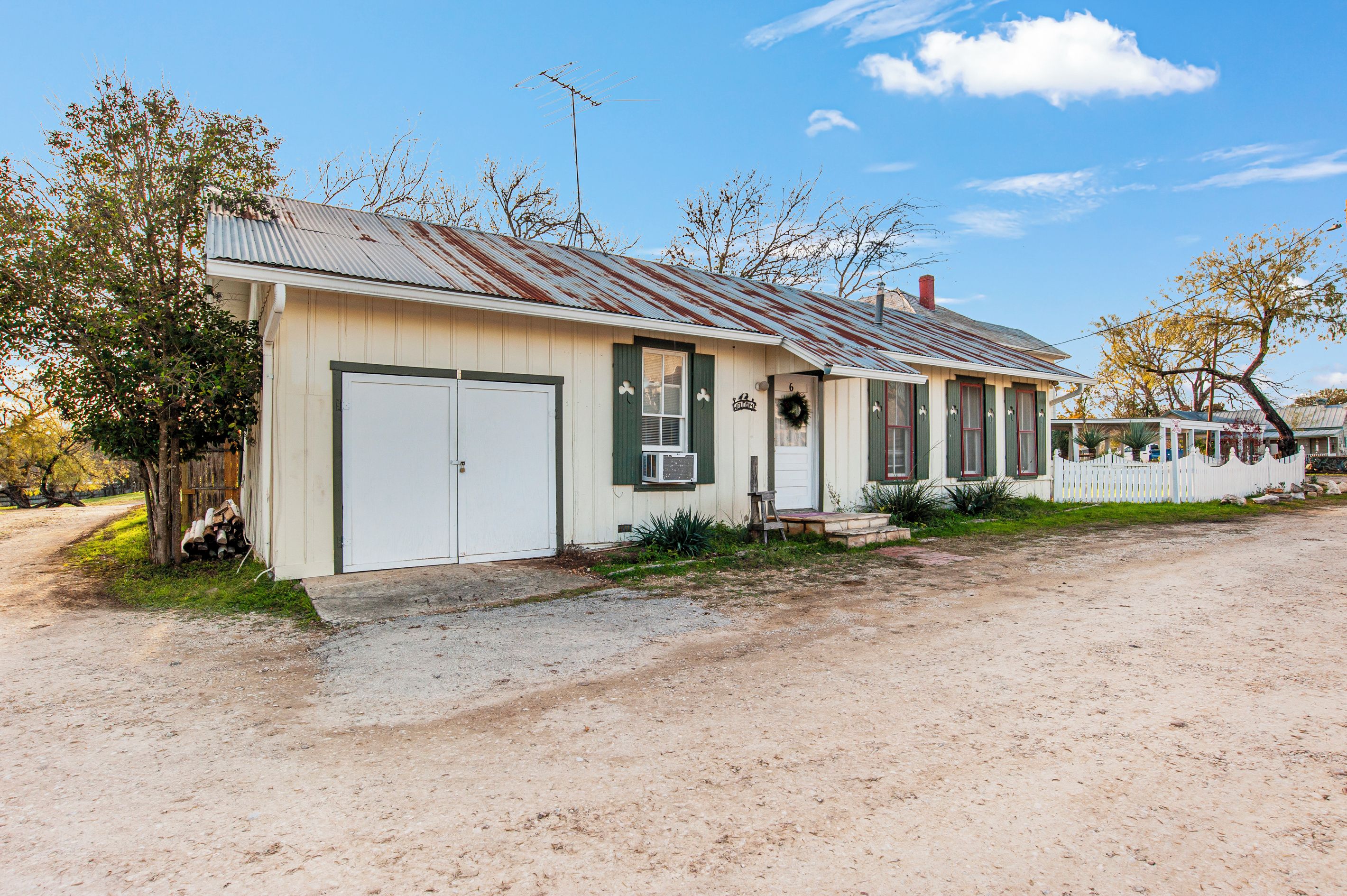 Ein eingeschossiges Gebäude mit Garage, einer Veranda mit Bank und einem kleinen Garten.