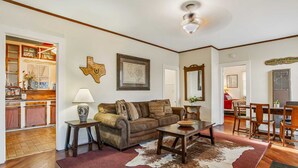 A living room with a brown leather sofa, a wooden coffee table, and a cowhide rug. There is a dining area with wooden chairs and a table. - Carriage Inn - Cottage (Bandera)