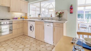Een moderne keuken met een vaatwasser, fornuis en gootsteen. Er is een raam met zonwering en een klok aan de muur.