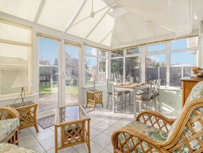Une véranda avec une table en verre dressée pour le repas, des meubles en osier et une vue sur le jardin arrière.