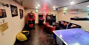A room with a ping pong table, arcade games, and a couch.