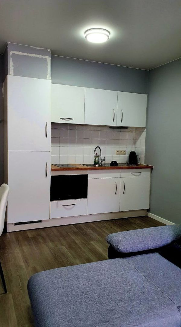 A compact kitchen with white cabinets, a wooden countertop, and a built-in oven.