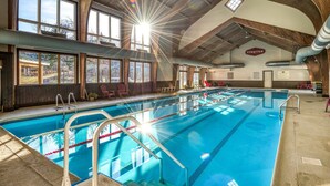 Una piscina interior con carriles delimitados, vigas de madera y vistas al exterior a través de amplias ventanas.