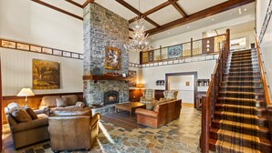 Un vestíbulo amplio con chimenea de piedra, mobiliario de cuero y una escalera de madera.