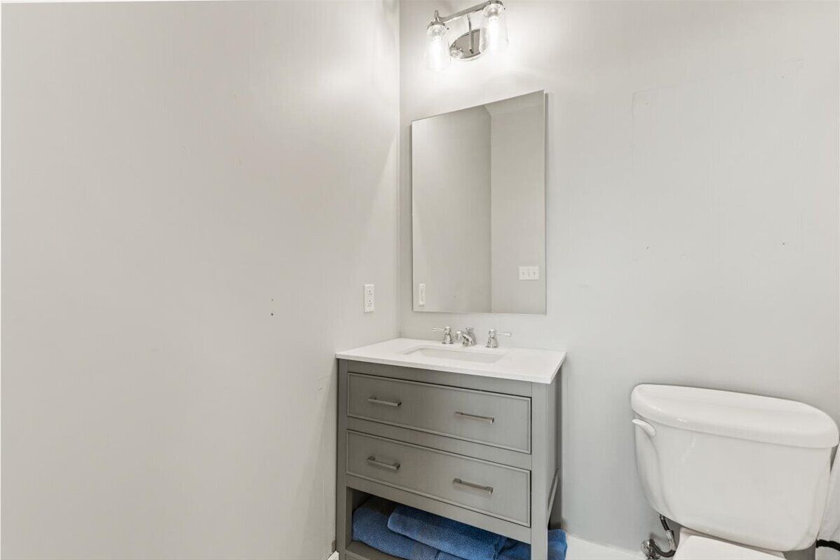 Baño con lavamanos blanco, espejo y retrete.