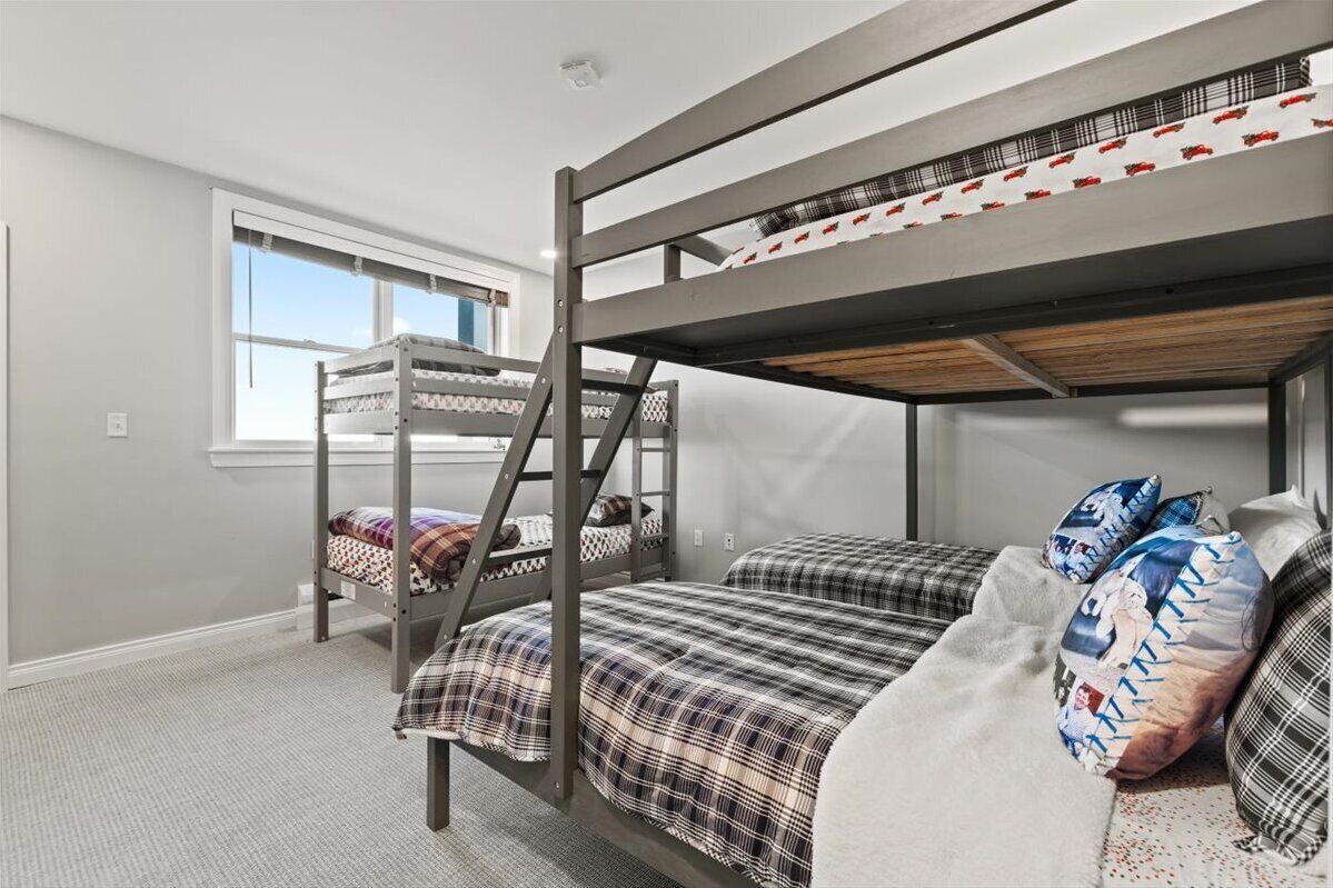 Une chambre avec un lit superposé, une fenêtre, un sol recouvert de moquette et un lit avec une couette à carreaux.