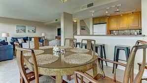 A modern living room with a glass dining table, wooden chairs, and a blue sofa. - Oceanview 4BR condo in Amelia Island Plantation with pool, pet friendly! (Fernandina Beach)