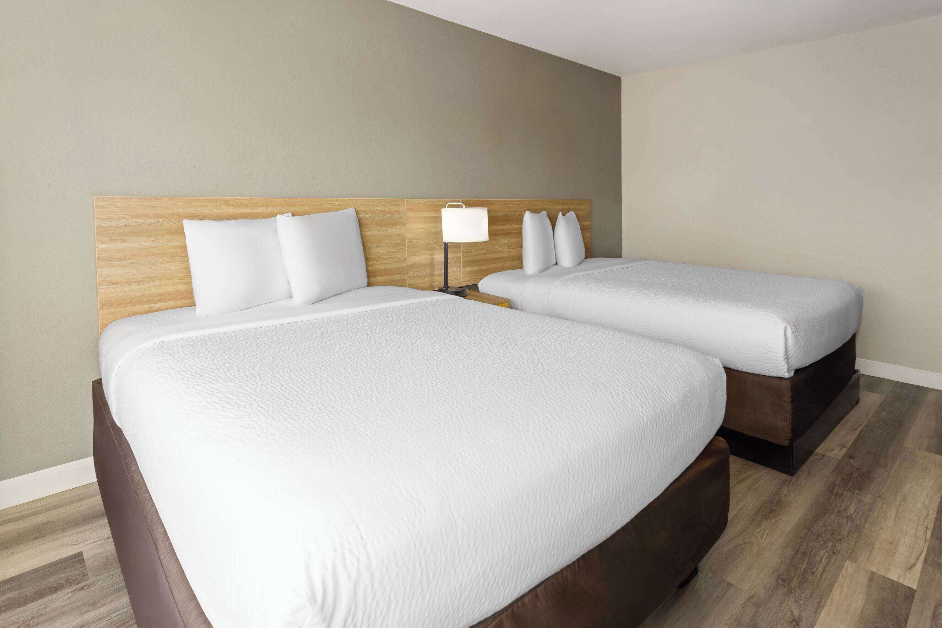 A hotel room with two beds, a wooden headboard, a nightstand with a lamp, and a wooden floor.