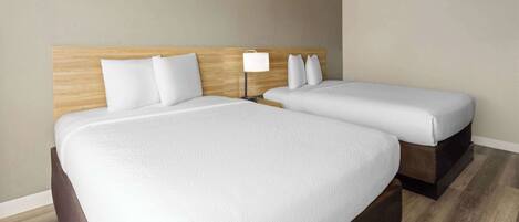 A hotel room with two beds, a wooden headboard, a nightstand with a lamp, and a wooden floor.