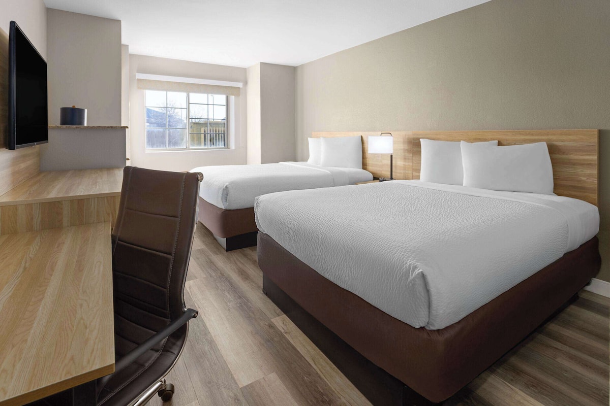 A hotel room with two beds, a desk, a chair, a TV, and a window with a view.