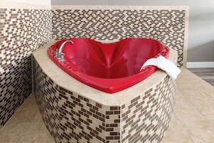 Una bañera de esquina con diseño de corazón, rodeada de paredes con mosaicos.