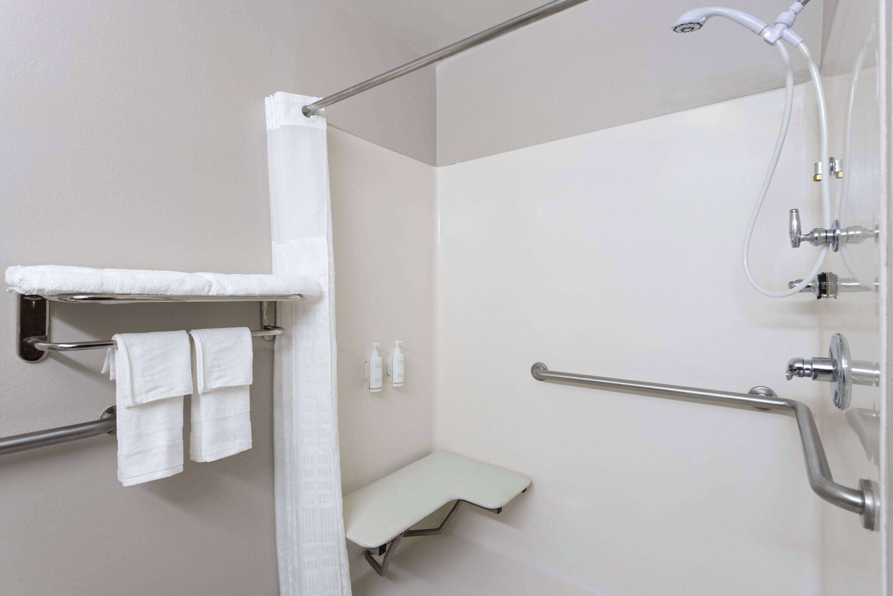 A bathroom with a shower, grab bars, a bench, and a towel rack.