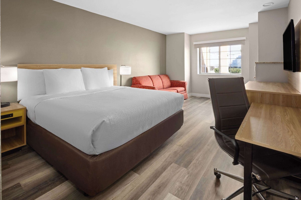 A hotel room with a large bed, a desk, a chair, and a TV.