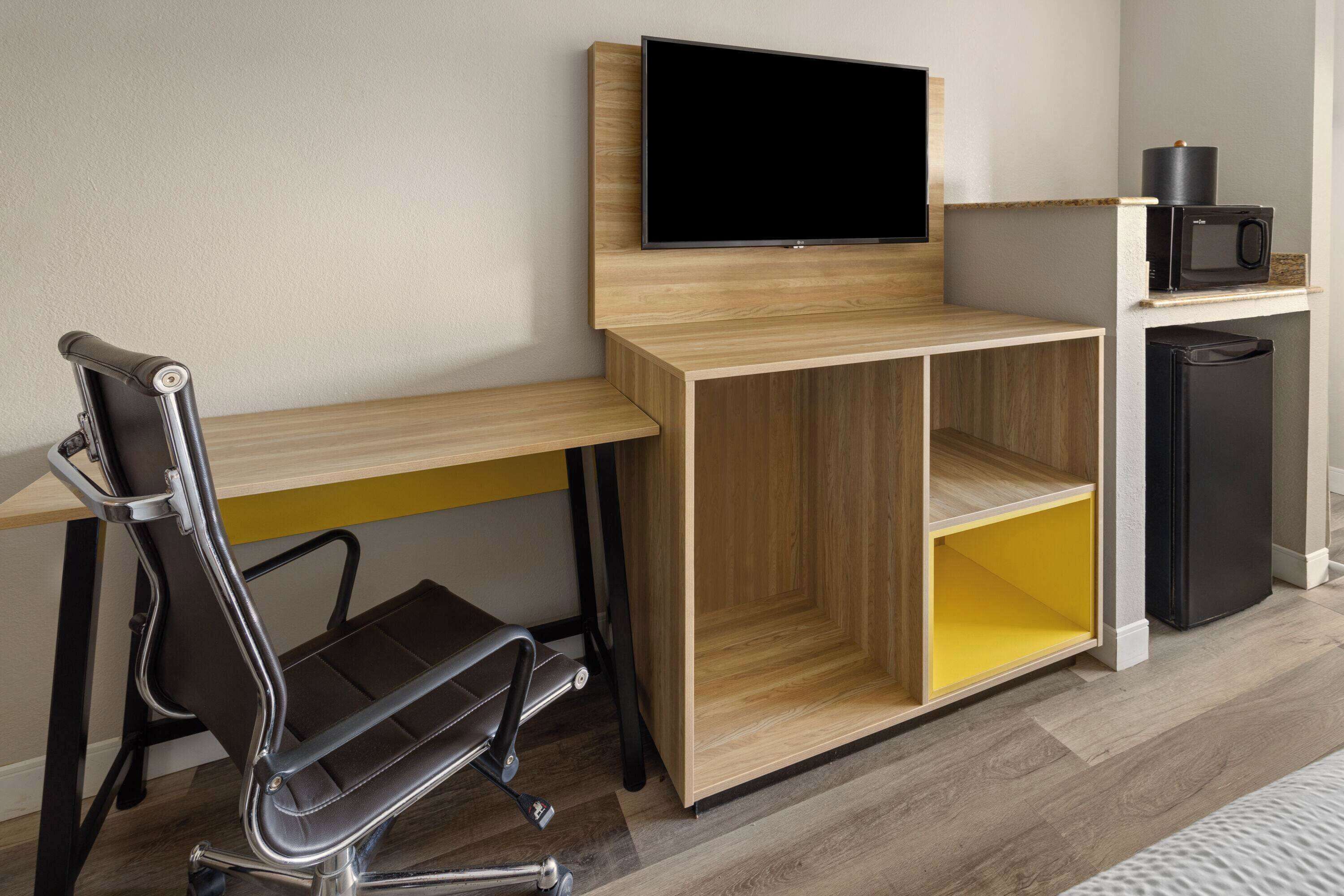 A modern office space with a desk, chair, TV, and a small kitchenette.