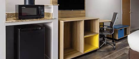 Une petite cuisine équipée d’un four à micro-ondes, d’un réfrigérateur et d’un téléviseur à écran plat fixé au-dessus d’un bureau en bois.