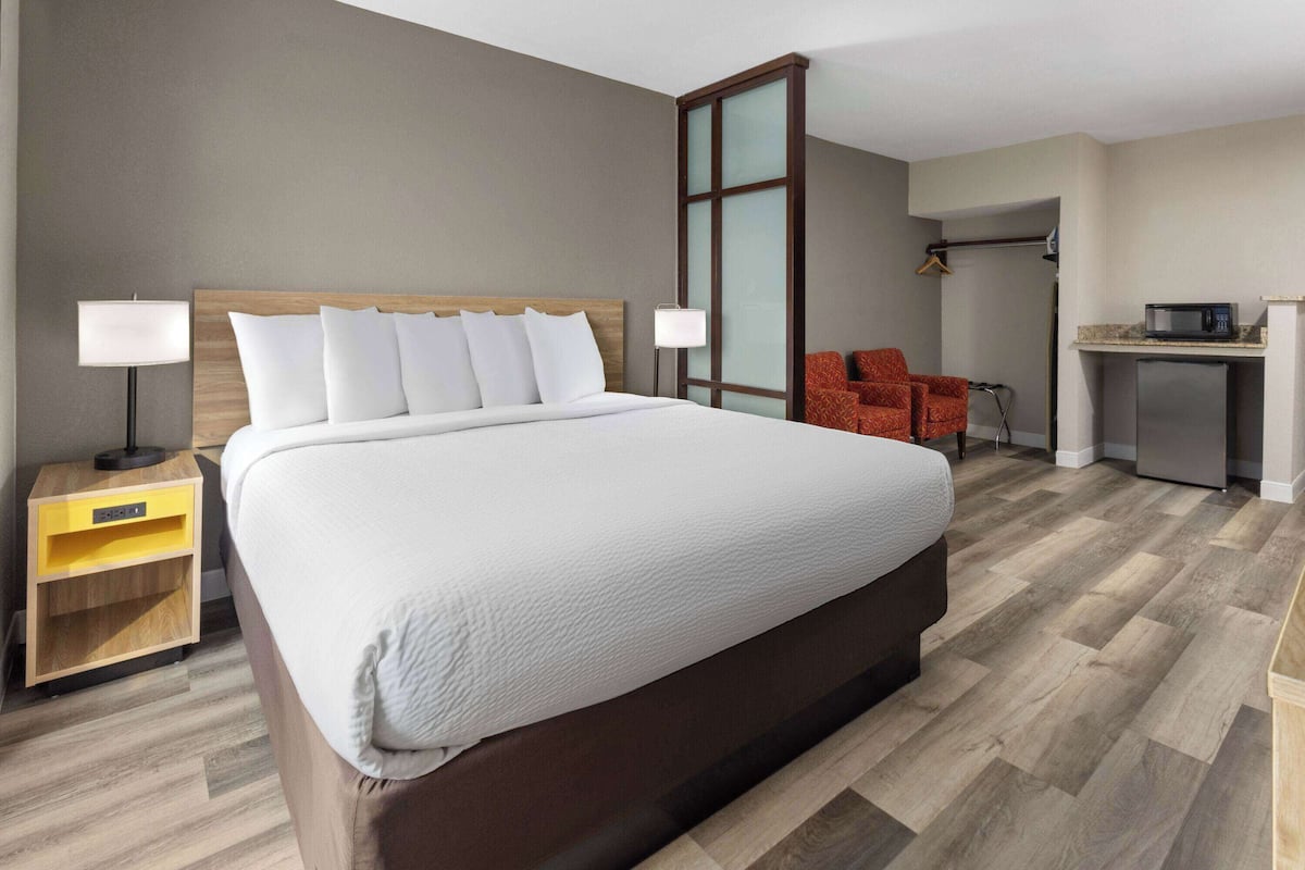 A hotel room with a large bed, a desk with a microwave, a chair, and a wardrobe.