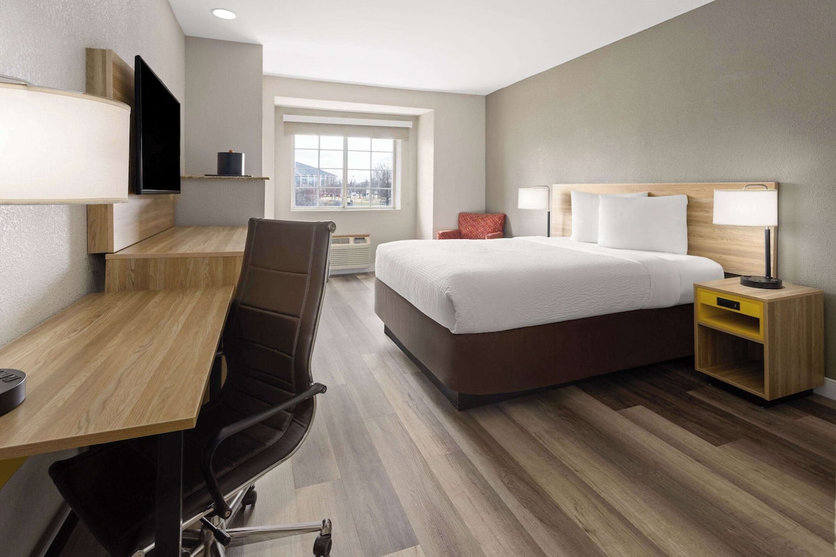 A hotel room with a bed, desk, chair, TV, bedside table, lamp, and a window with a view.
