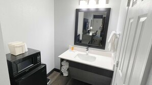 Un baño pequeño con un lavamanos blanco, un microondas negro y un espejo sobre el lavamanos.