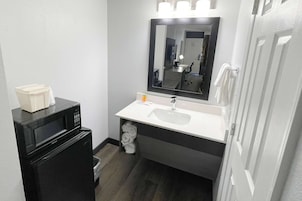 Un baño pequeño con un lavamanos blanco, un microondas negro y un espejo sobre el lavamanos.