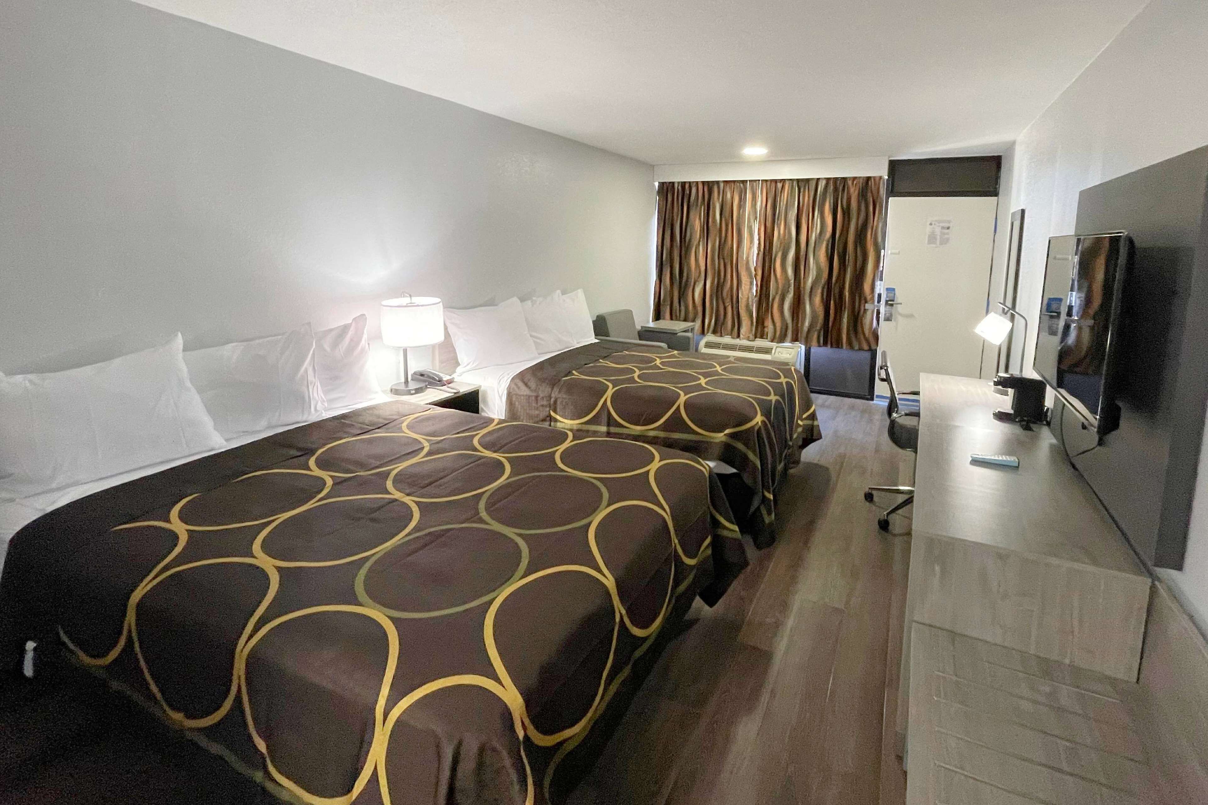 Quarto de hotel com duas camas, uma escrivaninha, televisão e banheiro.
