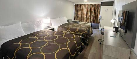 A hotel room with two beds, a desk, a TV, and a bathroom.
