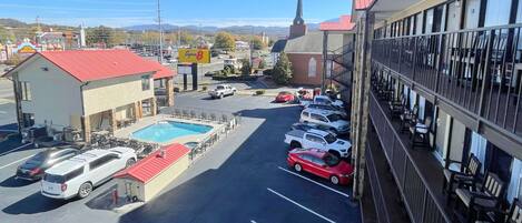 A hotel with a swimming pool, a parking lot with several cars, and a view of a church steeple in the background.