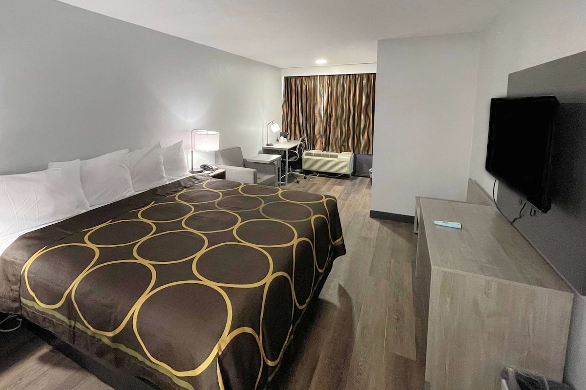 A hotel room with a bed, desk, chair, lamp, air conditioning unit, and a television.