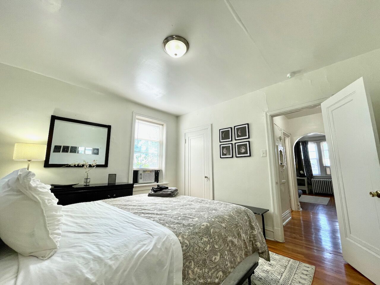 Een slaapkamer met een bed, een dressoir, een spiegel en een deur naar een andere kamer.