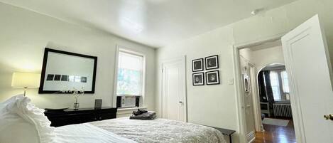 Een slaapkamer met een bed, een dressoir, een spiegel en een deur naar een andere kamer.