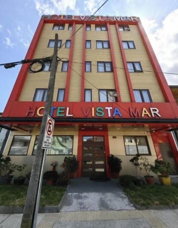 A multi-story hotel with a red and beige facade, featuring the name 'HOTEL VISTA MAR' prominently displayed.