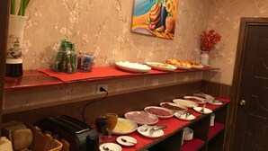 A buffet setup with various food items and condiments on red trays, a painting on the wall, and a door in the background. - HOTEL VISTA MAR (Puerto Montt)