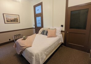Hotellihuone, jossa on sänky, tuoli, ovi ja seinälle ripustettu taideteos.
