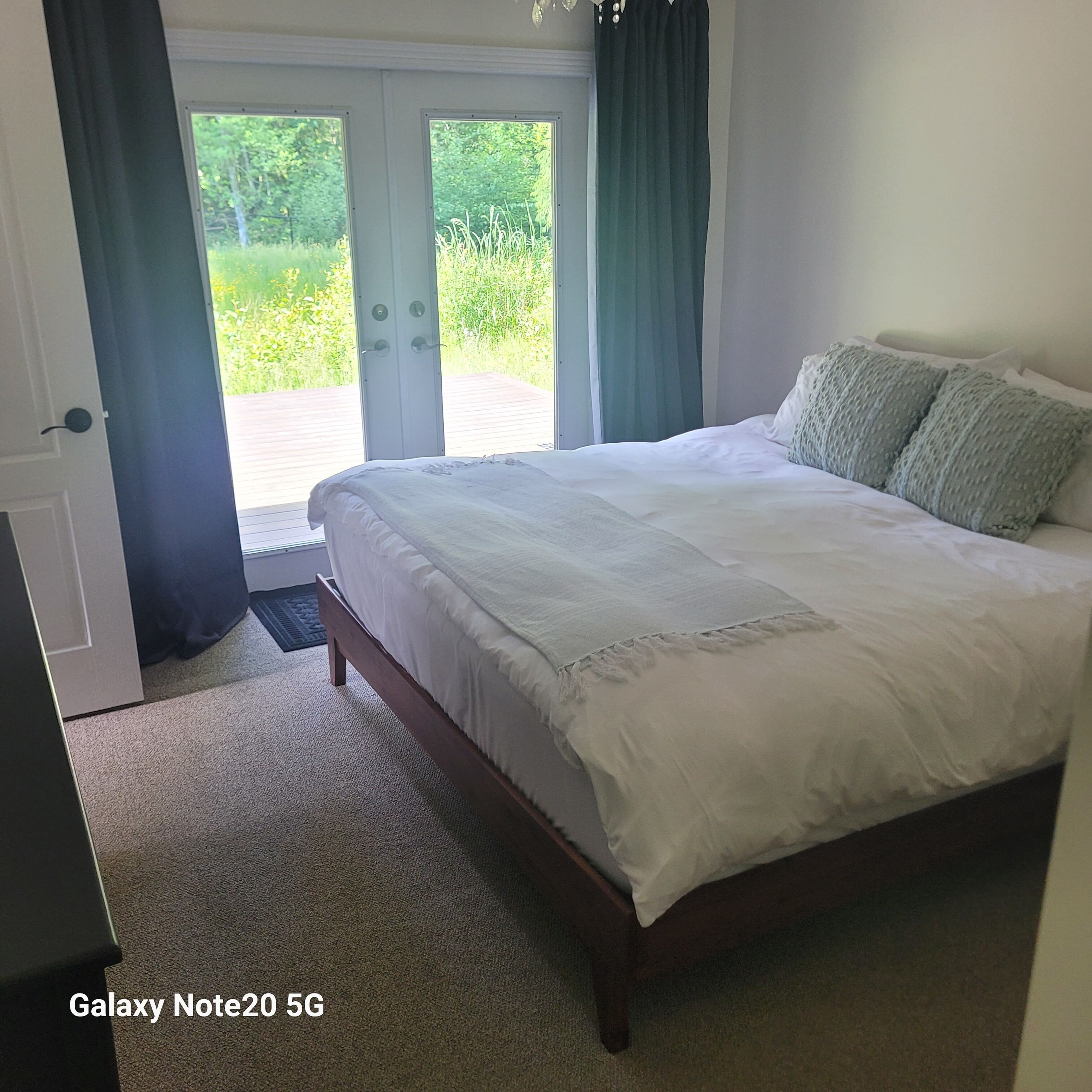 Un dormitorio con una cama grande, una puerta que da a un balcón y un teléfono Galaxy Note20 5G en el suelo.