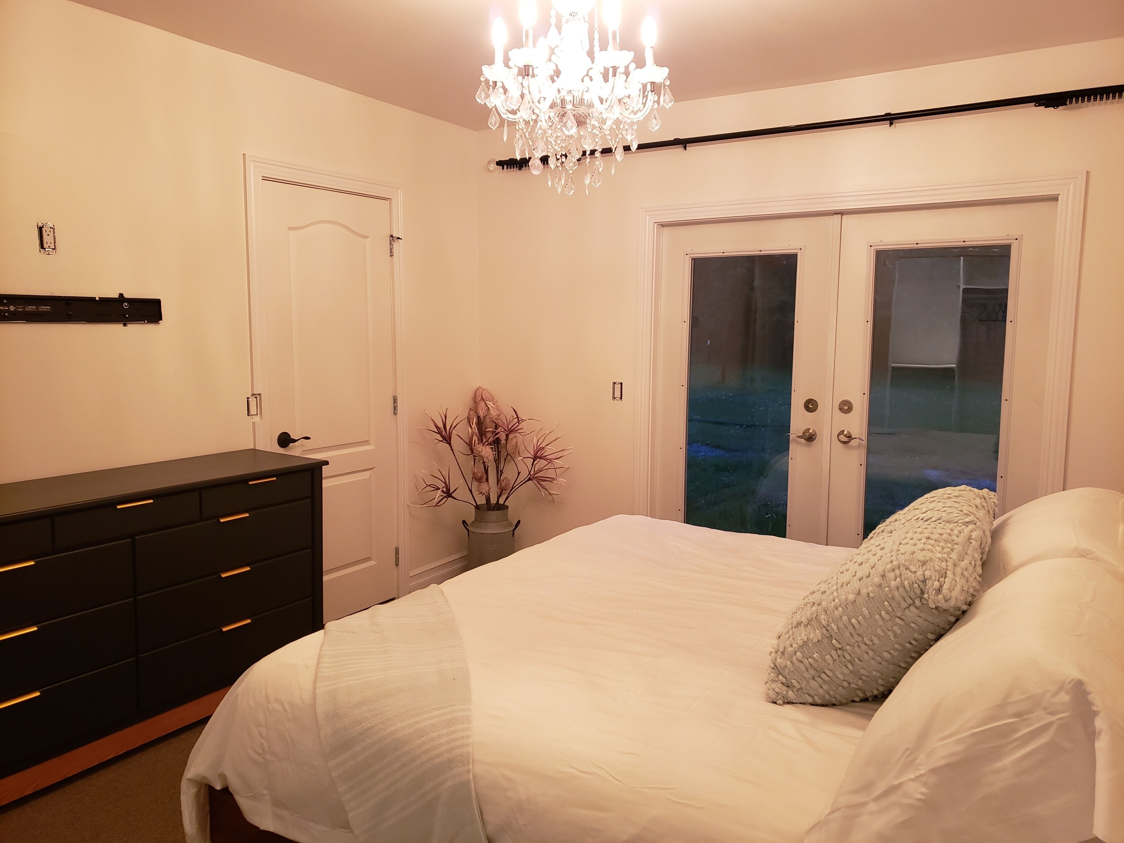 Un dormitorio con cama, cómoda, lámpara de araña y puerta con paneles de vidrio esmerilado.