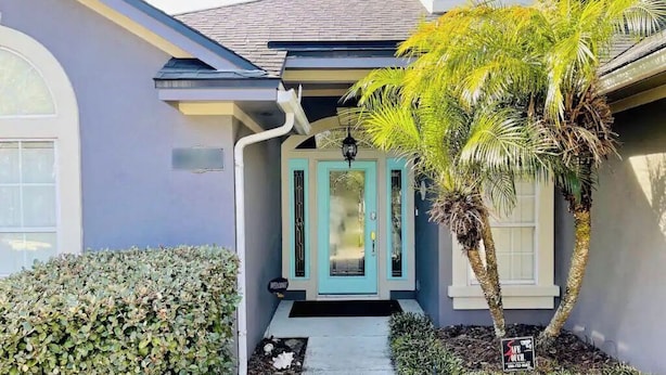 Une maison avec une porte d’entrée de couleur turquoise, un petit porche et un palmier.