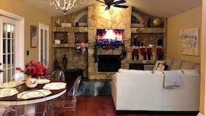 Un salon chaleureux avec une cheminée en pierre, un ventilateur de plafond et un téléviseur fixé au-dessus.