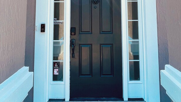 A two-story building with a dark front door, white trim, and a small window above the door.