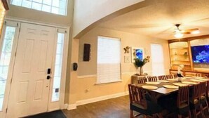 A spacious dining area with a high ceiling fan, wooden flooring, and a large window providing natural light.