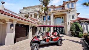 A large, two-story house with a red-tiled roof, a covered driveway, and a golf cart parked in front. - Private heated pool, Luxury Mediterranean Mansion sleeps 16 (Destin)
