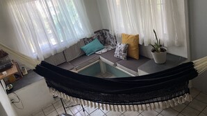 A hammock chair with a black and white patterned cushion, a potted plant, and sheer white curtains in a room with tiled flooring. - Apartment with pool 10 minutes from Playa Chahue (Crucecita)