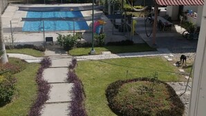 A swimming pool with a clear view of the surrounding area, including a grassy lawn, a pathway, and a small garden with flowers. - Apartment with pool 10 minutes from Playa Chahue (Crucecita)