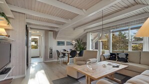 Amplia sala de estar con techo de madera, un sofá, una mesa de centro y un comedor con sillas y una mesa.