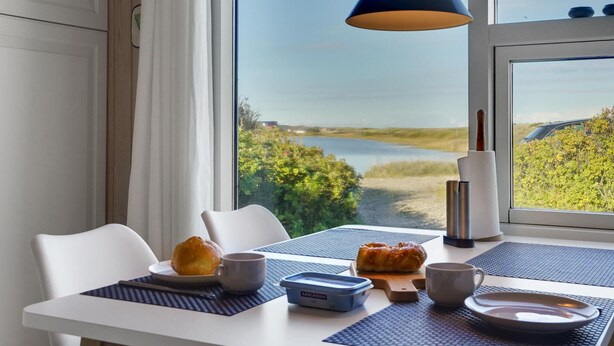 Una mesa de comedor con vista a un lago y follaje, una lámpara azul y alimentos para el desayuno.