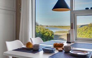 Una mesa de comedor con vista a un lago y follaje, una lámpara azul y alimentos para el desayuno.